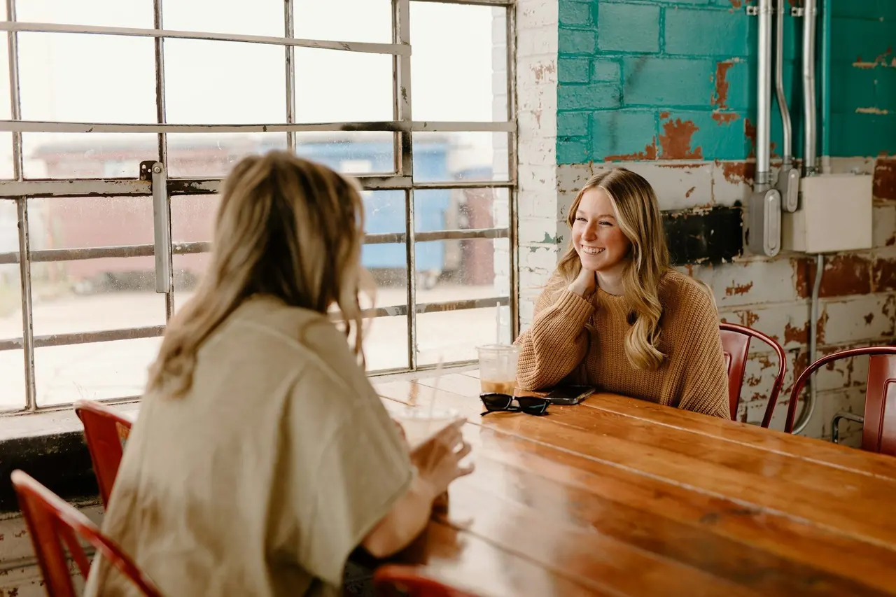 Duas mulheres conversando com calma e sorrindo em uma mesa de madeira